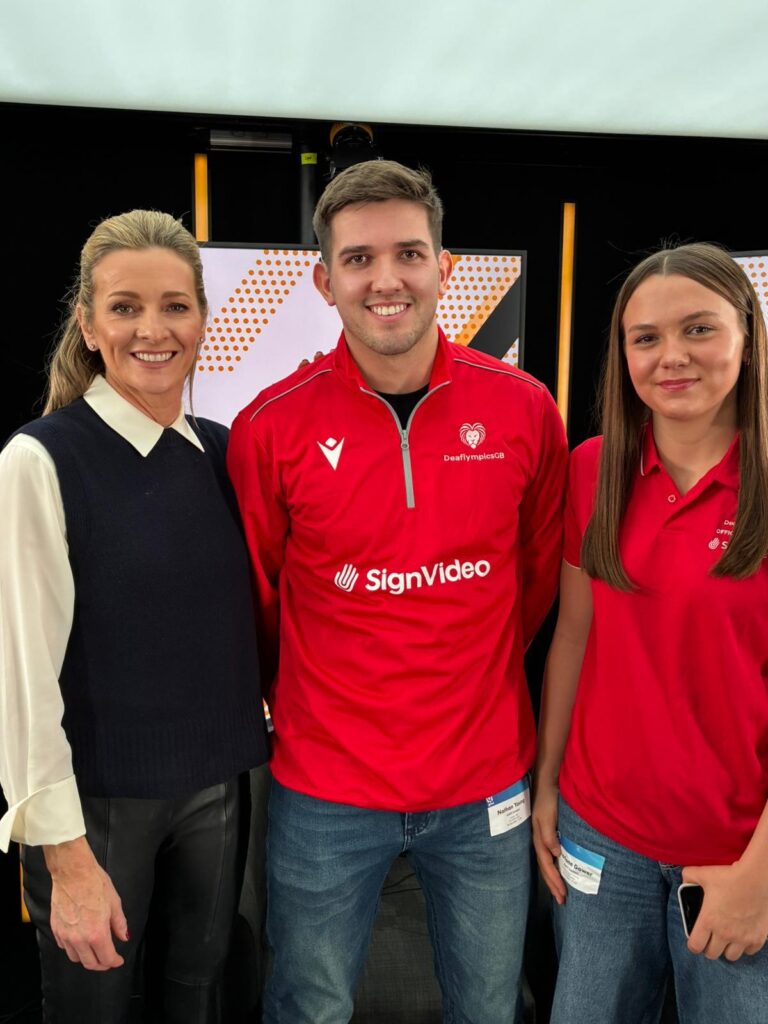 Host Gabby Logan stands with athletes Nathan Young and Charlotte All three are smiling at the camera and Charlotte and Nathan are wearing their DeaflympicsGB kit